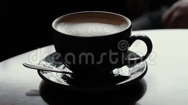特写男士手拿一杯咖啡，咖啡屋里的木桌上放着牛奶